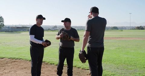 Baseball coaches discussing strategy on sunlit infield during adult recreational practice