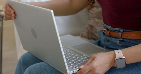 African american woman working on laptop on couch wearing smartwatch and denim jeans