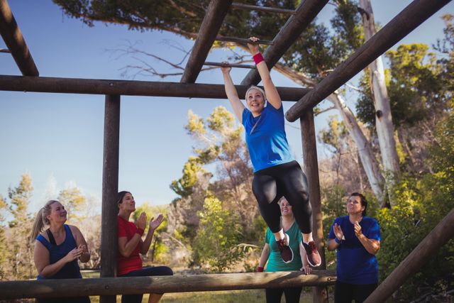 Woman being cheered bye her teammates to climb monkey bars during obstacle course training in the boot camp