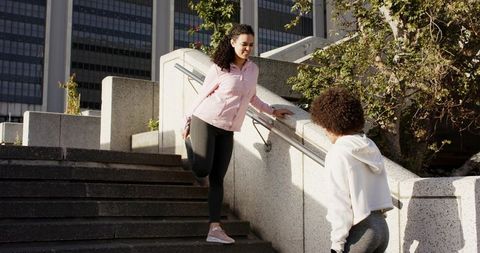 Urban workout partners stretching on concrete steps holding metal handrail before run