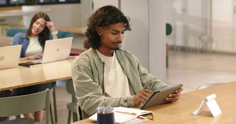 African american male student studying on tablet while female peer works on laptop
