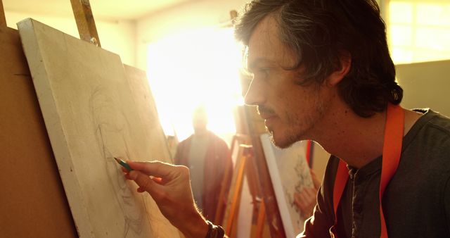 Artist concentrating on a sketch in an art studio with sunlight filtering through the window. Might be used for topics related to creativity, artistic expression, and art education.
