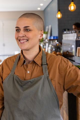 Smiling female barista serving customers at cozy cafe counter with pastry display