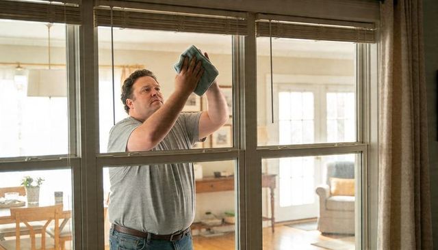 Man cleaning large living room window with microfiber cloth for home chores in sunlit home