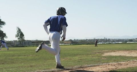 Youth baseball player running on field under sunny sky