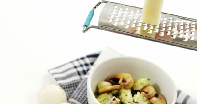 Close-up of hand grating cheese over bowl of fresh mushroom pasta in kitchen. This image is great for recipes, food blogs, cooking classes, culinary websites, and advertisements for kitchen tools and ingredients.