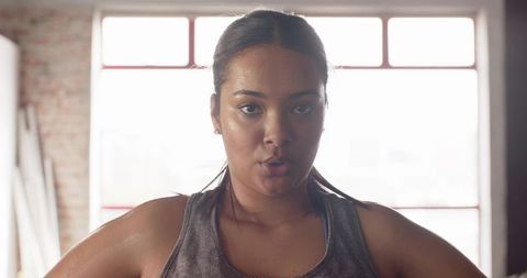 Determined woman finishing intense workout in backlit gym, sweating and focused