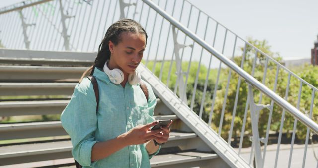 Young man using smartphone with headphones on neck outdoors - Download Free Stock Images Pikwizard.com