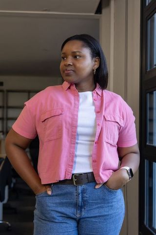 Confident african american woman standing by window in modern office wearing pink shirt