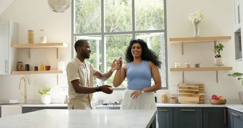 Couple dancing and laughing in bright modern kitchen while meal planning together