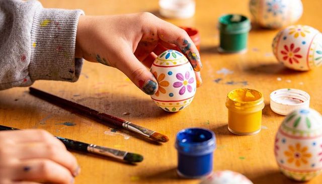 Child decorating hand-painted floral easter eggs with bright craft paints and brushes diy