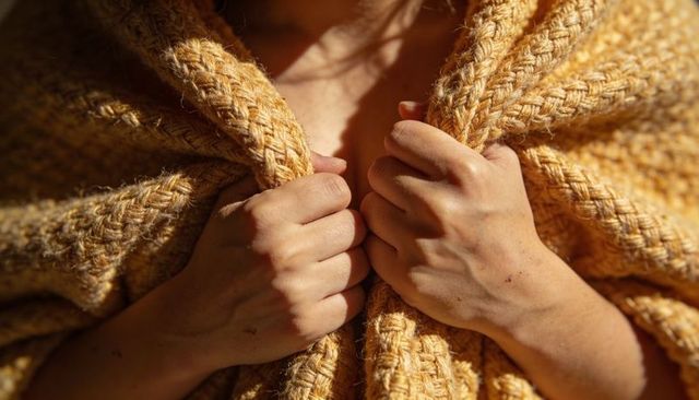 Wrapping in mustard yellow knit blanket, hands gripping chunky texture closeup for warmth