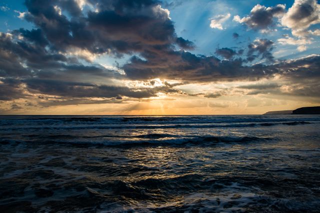 Sunset over the ocean with dramatic dark clouds and light shining through the horizon. Ideal for use in travel magazines, nature blogs, inspirational posters, and as background images for websites or presentations. Perfect for conveying tranquility, beauty, and the majesty of nature.