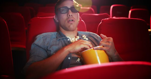Man wearing 3D glasses and eating popcorn in movie theater. Ideal for themes related to entertainment, leisure activities, cinema experiences, or promotional materials for movie screenings and theater advertisements.