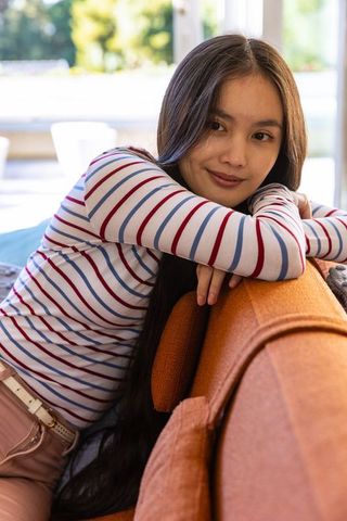 Asian Woman Seated Comfortably on Orange Couch with Natural Light