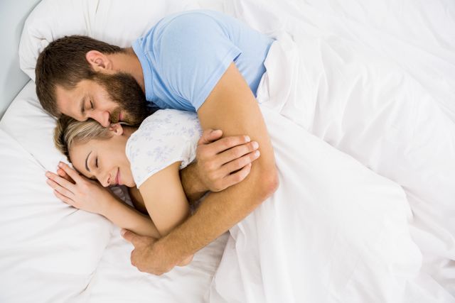 Man embracing woman while sleeping on bed at bedroom