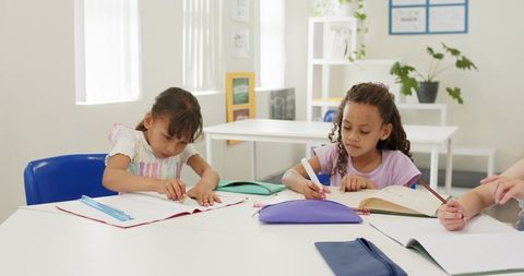 African american girls writing and studying together at classroom table with supplies