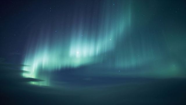 Teal auroral curtains dancing across polar night sky, stars veiling horizon mist