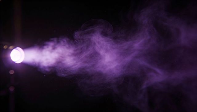 Purple spotlight projecting through dense smoke plume on dark stage casting dramatic glow