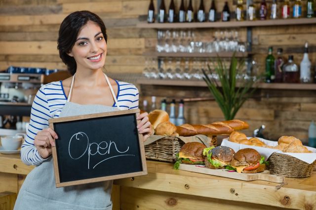 Portrait of waitress holding open signboard at counter in cafÃ©