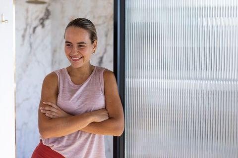 Smiling athletic woman leaning on ribbed glass partition in minimalist wellness studio