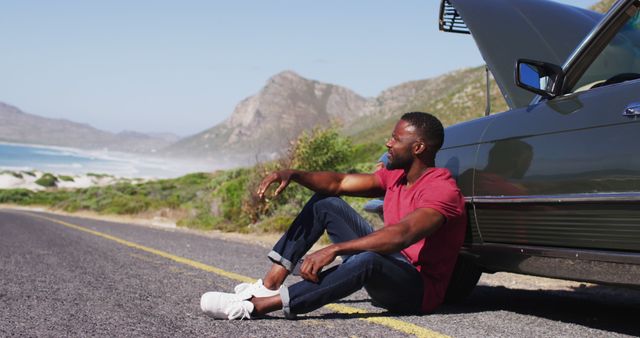 African american man sitting near his broken down car on road. road trip travel and adventure concept