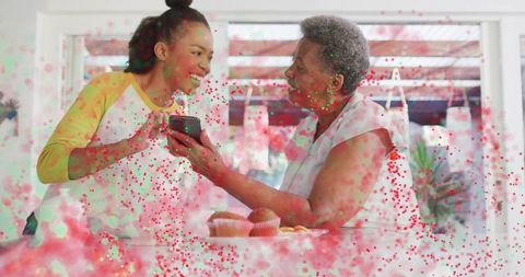 Sunlit kitchen bonding: young woman sharing smartphone with senior while baking together