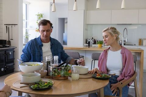 Couple sharing healthy salad at round dining table in bright modern kitchen