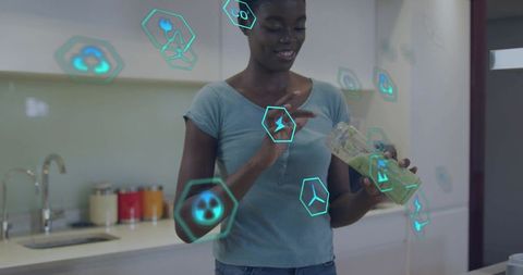 Woman interacting with augmented reality icons while pouring green smoothie in kitchen