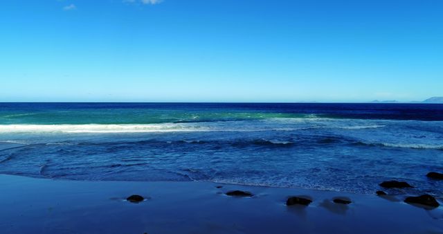 Gentle waves wash onto a sandy shore under a vast blue sky, with copy space - Download Free Stock Photos Pikwizard.com