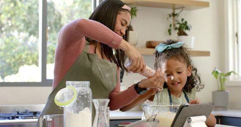 Mother and daughter baking together in home kitchen using tablet for recipe guidance