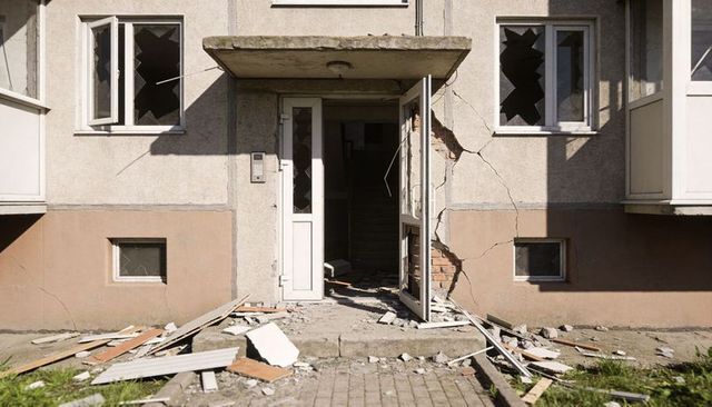 Opening white door revealing dark staircase in damaged apartment with shattered windows