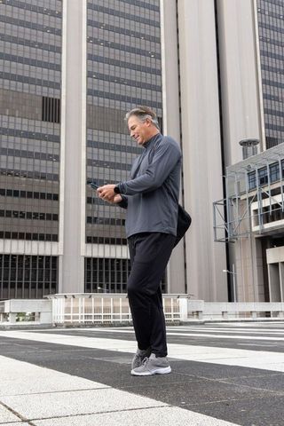 Middle-aged man checking smartphone on rooftop plaza with city skyscrapers