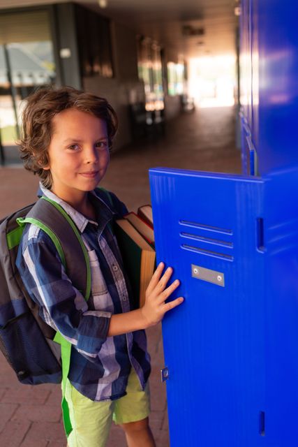 Young Caucasian boy opening his locker in a school hallway, smiling and holding books. Ideal for educational materials, back-to-school promotions, and articles about student life.