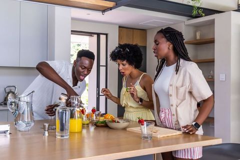 African american friends mixing colorful drinks at sunlit modern kitchen island