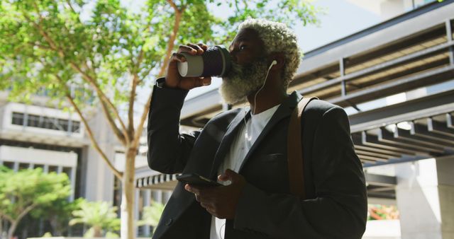 African american senior man drinking coffee and using smartphone in corporate park. active senior lifestyle living concept