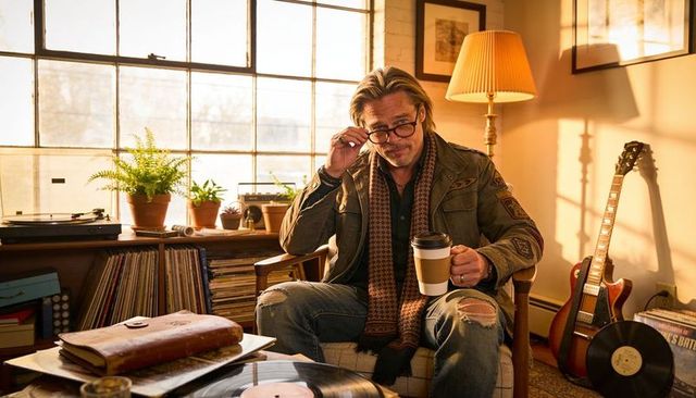 Midlife man lifting glasses while holding coffee cup in sunlit home studio with vinyl and guitar