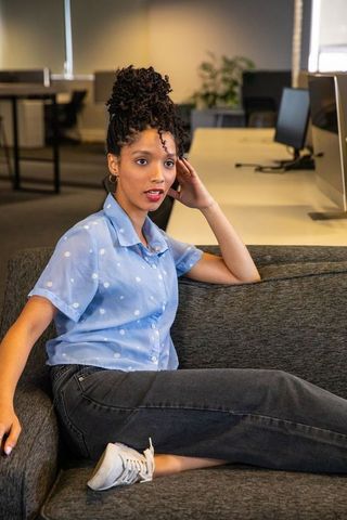African american woman relaxing on sofa wearing polka dot blouse in modern open office