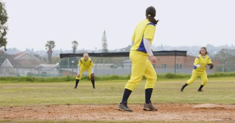 Female softball players in yellow uniforms on mound during pitch