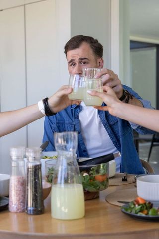 Friends clinking glasses around casual home dinner featuring lemonade and fresh salad
