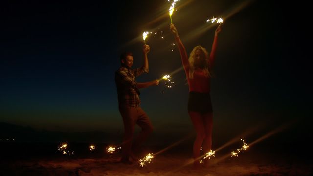 Young couple enjoying a romantic and fun-filled evening on a beach while dancing with sparklers at dusk. Perfect for themes related to celebrations, summer fun, beach parties, romantic getaways, and happy moments. Ideal for advertising travel destinations, celebratory events, and lifestyle blogs.