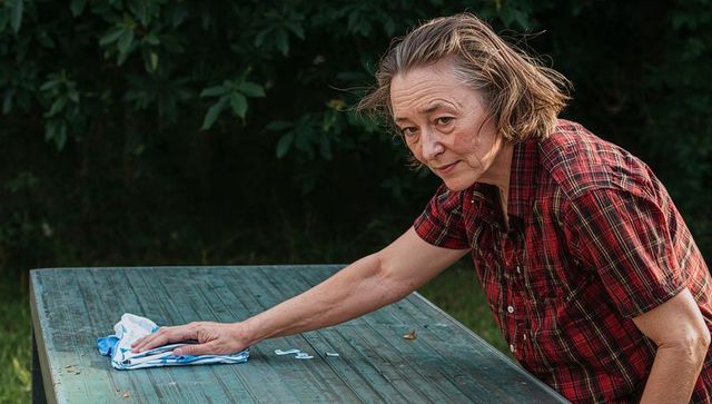 Senior woman cleaning weathered outdoor table in garden, caring household chores, home care