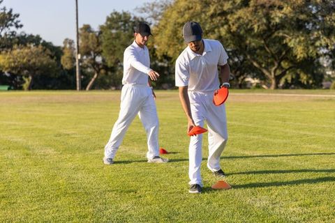 Cricket players placing orange cones on grass pitch wearing white kit practicing drills and teamwork