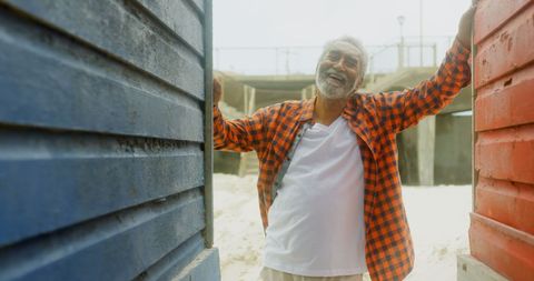 Smiling Elderly Man Standing Between Colorful Beach Huts on Sunny Day