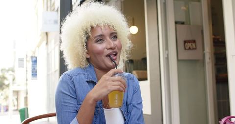 Happy Woman with Curly Hair Enjoying Drink at Outdoor Cafe