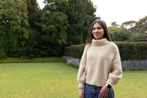 Young asian woman standing in garden wearing cream sweater and smartwatch, calm