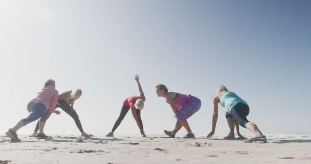 Group of elderly women dressed in workout attire, conducting stretching exercises on beach with clear blue sky. This imagery can be used to portray active senior lifestyle, group fitness sessions, or beach workout routines. Ideal for use in healthcare, wellness, fitness industry marketing, or senior-focused lifestyle publications.
