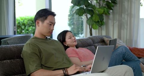 Couple working and relaxing with laptop and tablet on modern sofa in sunlit living room