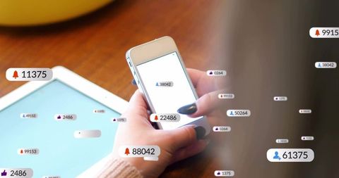 Hands holding smartphone scrolling social media notifications on wooden table with tablet