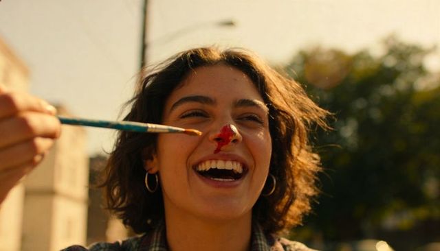 Young woman laughing with red paint on nose while friend dabbing paint with blue brush
